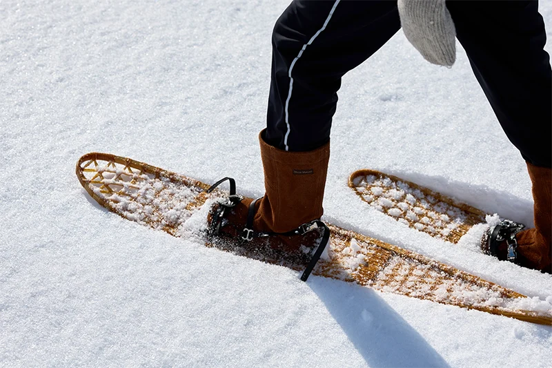 Person walking in wooden snowshoes across deep snow